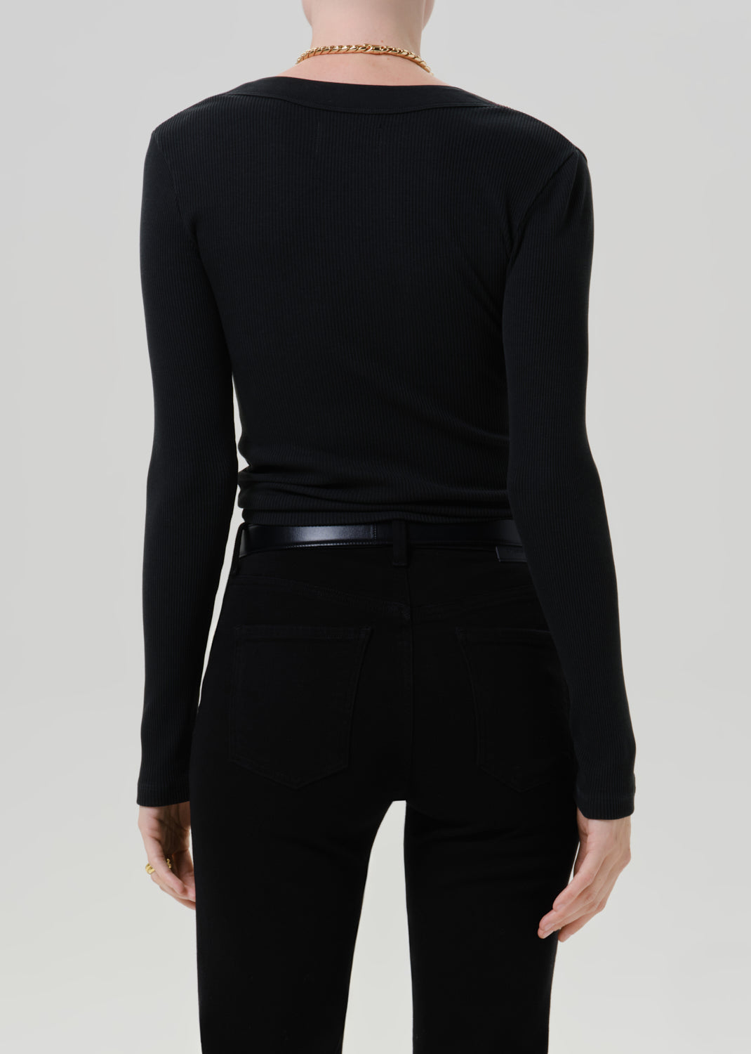 Person wearing a black long sleeve henley top with black pants viewed from the back on a grey background
