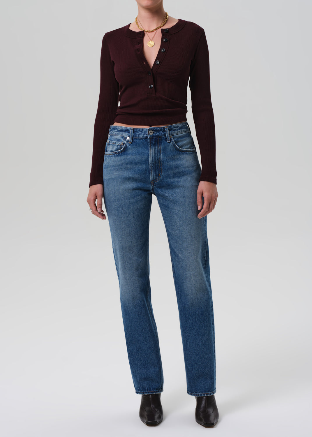 Person wearing a brown long-sleeve top and blue jeans on a white background