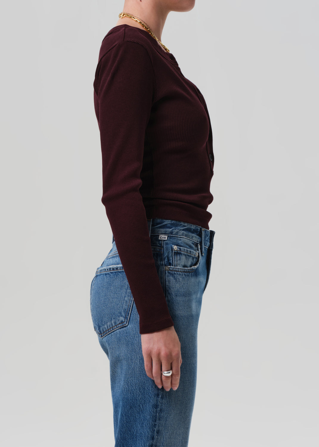 Person wearing a burgundy long-sleeve top and blue jeans on a light gray background