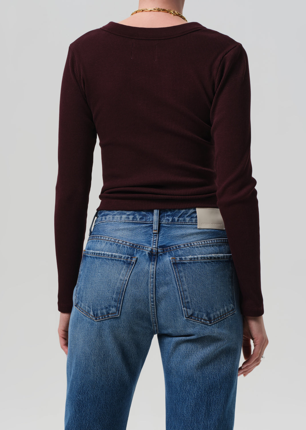 Person wearing a burgundy long-sleeve top and blue jeans on a plain background