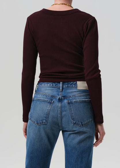 Person wearing a burgundy long-sleeve top and blue jeans on a plain background