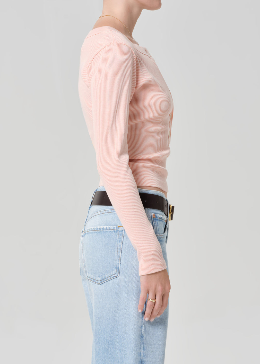 Person wearing a light pink long-sleeve shirt and light blue jeans with a brown belt.