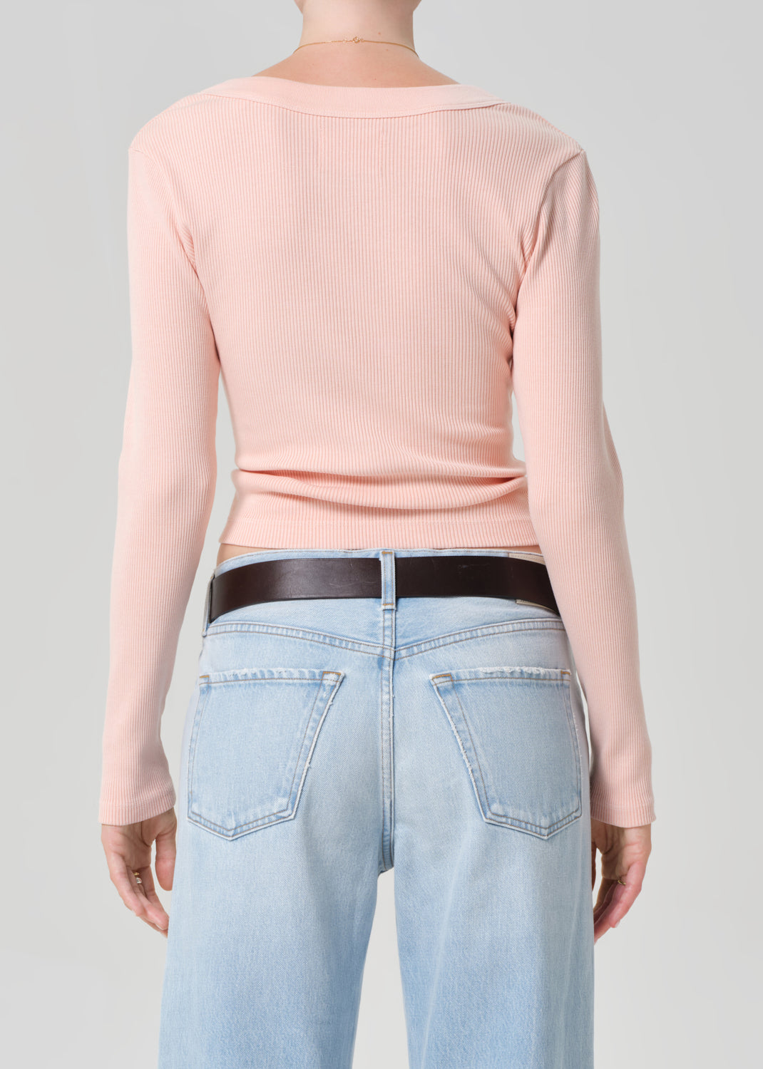 Person wearing a light pink long-sleeve shirt and light blue jeans with a brown belt.