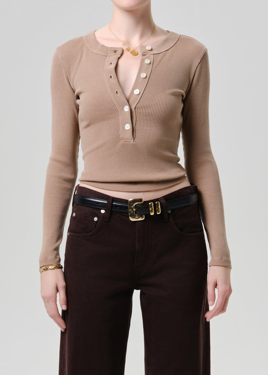 Person wearing a brown ribbed long-sleeve top and dark pants on a grey background