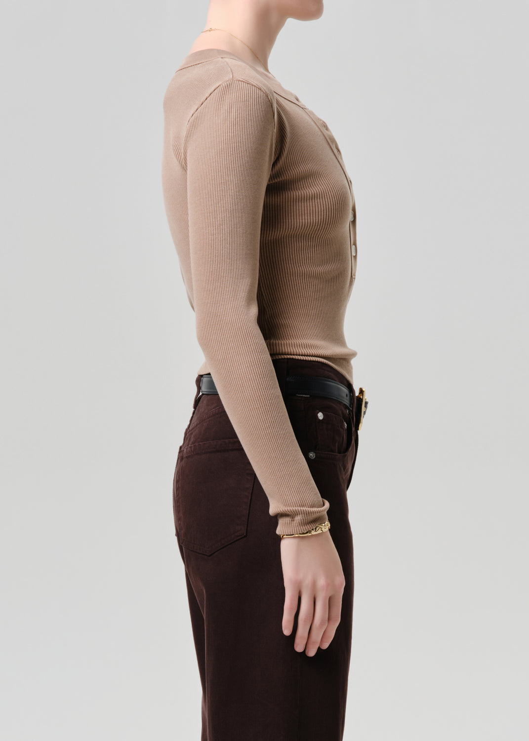 Person wearing a brown long-sleeve top and dark pants on a grey background