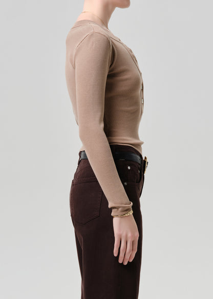 Person wearing a brown long-sleeve top and dark pants on a grey background