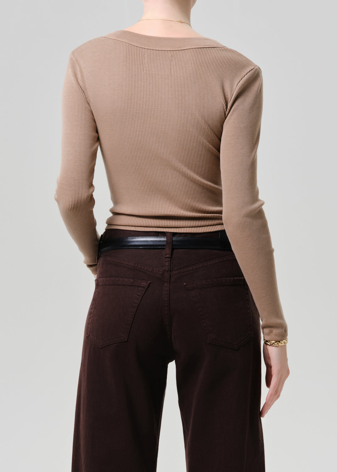 Person wearing a beige ribbed sweater and brown pants on a grey background