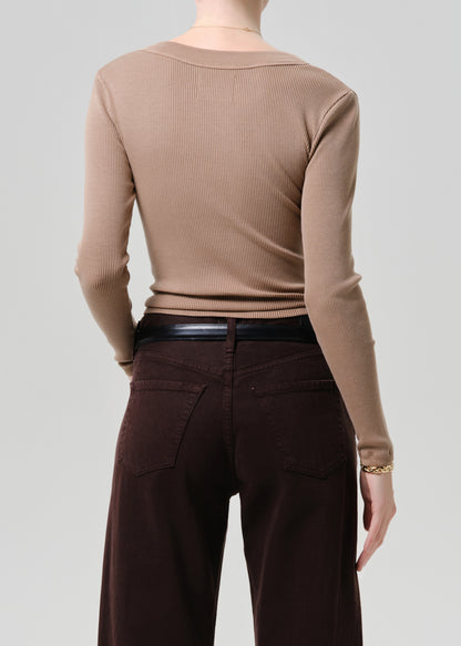 Person wearing a beige ribbed sweater and brown pants on a grey background
