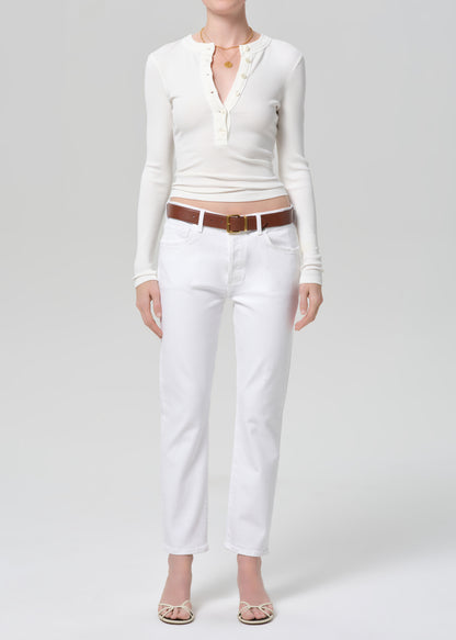 Person wearing a white long-sleeve top and white jeans with a brown belt on a gray background