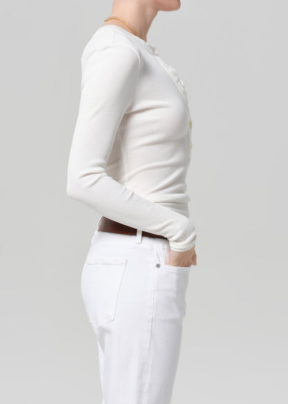 Person wearing a white long-sleeve top and white jeans with a brown belt on a gray background