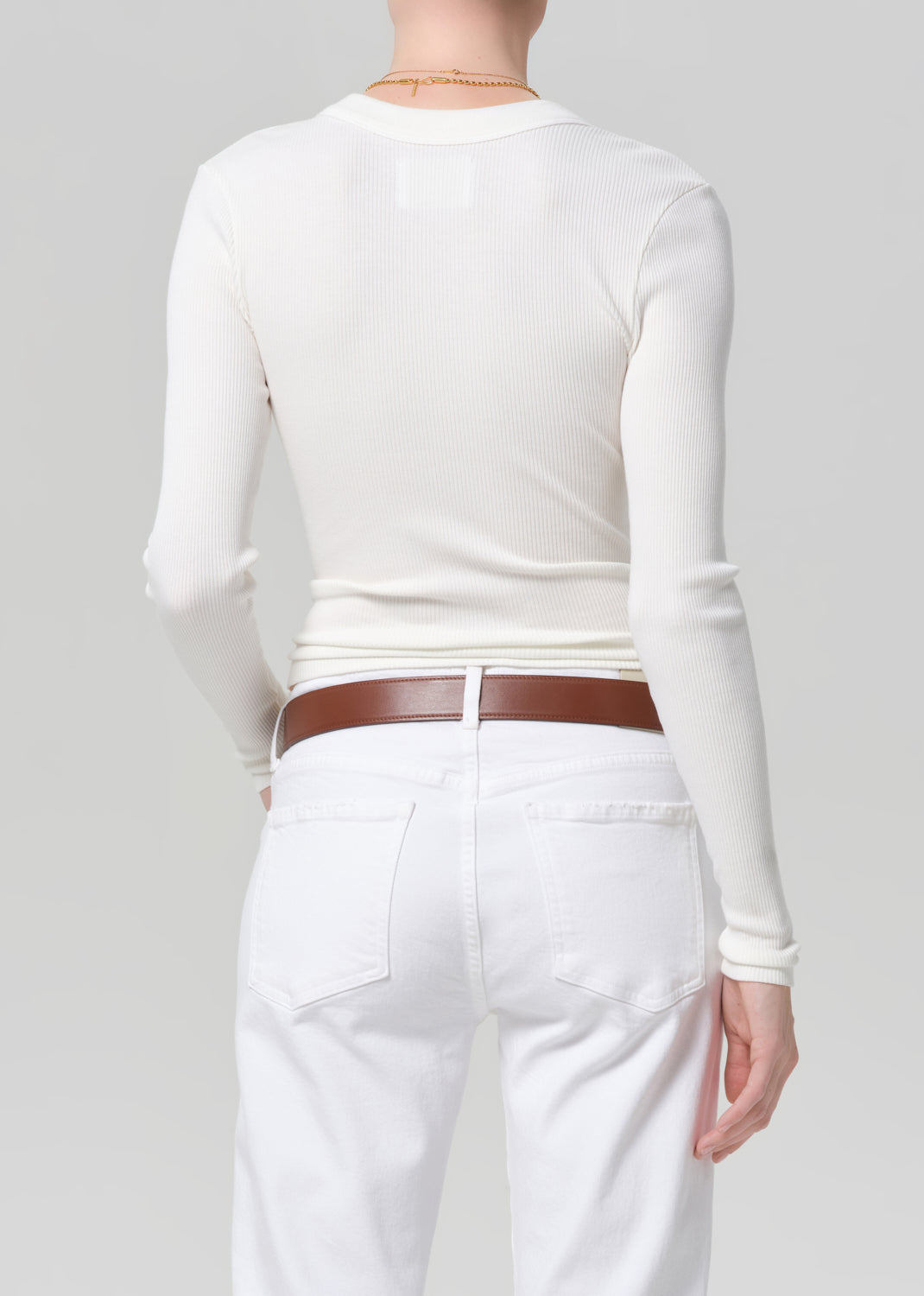 Person wearing a white long-sleeve top and white jeans with a brown belt on a gray background
