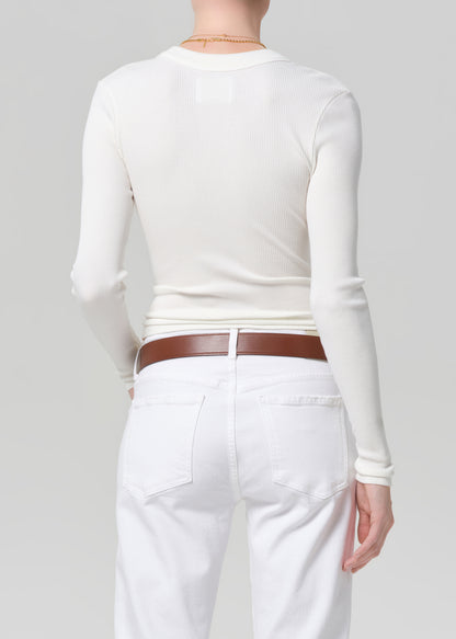 Person wearing a white long-sleeve top and white jeans with a brown belt on a gray background