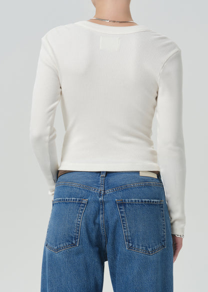 A person shown from the back wearing a fitted off-white ribbed long-sleeve top and blue jeans against a grey background.
