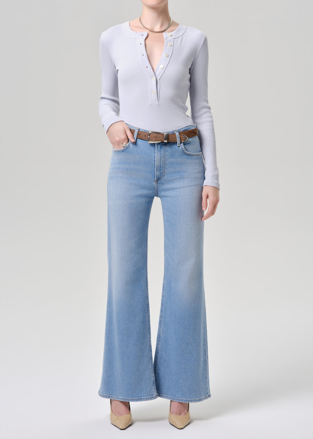 Person wearing a light blue long-sleeve top and light blue flared jeans on a grey background
