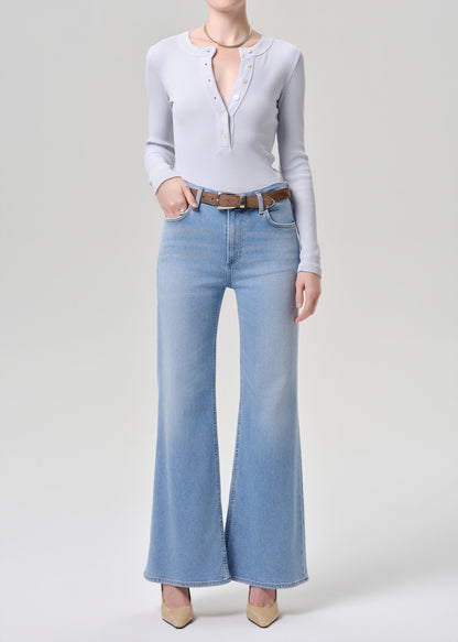 Person wearing a light blue long-sleeve top and light blue flared jeans on a grey background