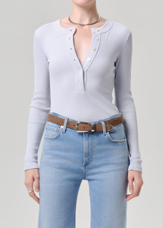 Person wearing a light blue long-sleeve top and blue jeans with a brown belt on a grey background