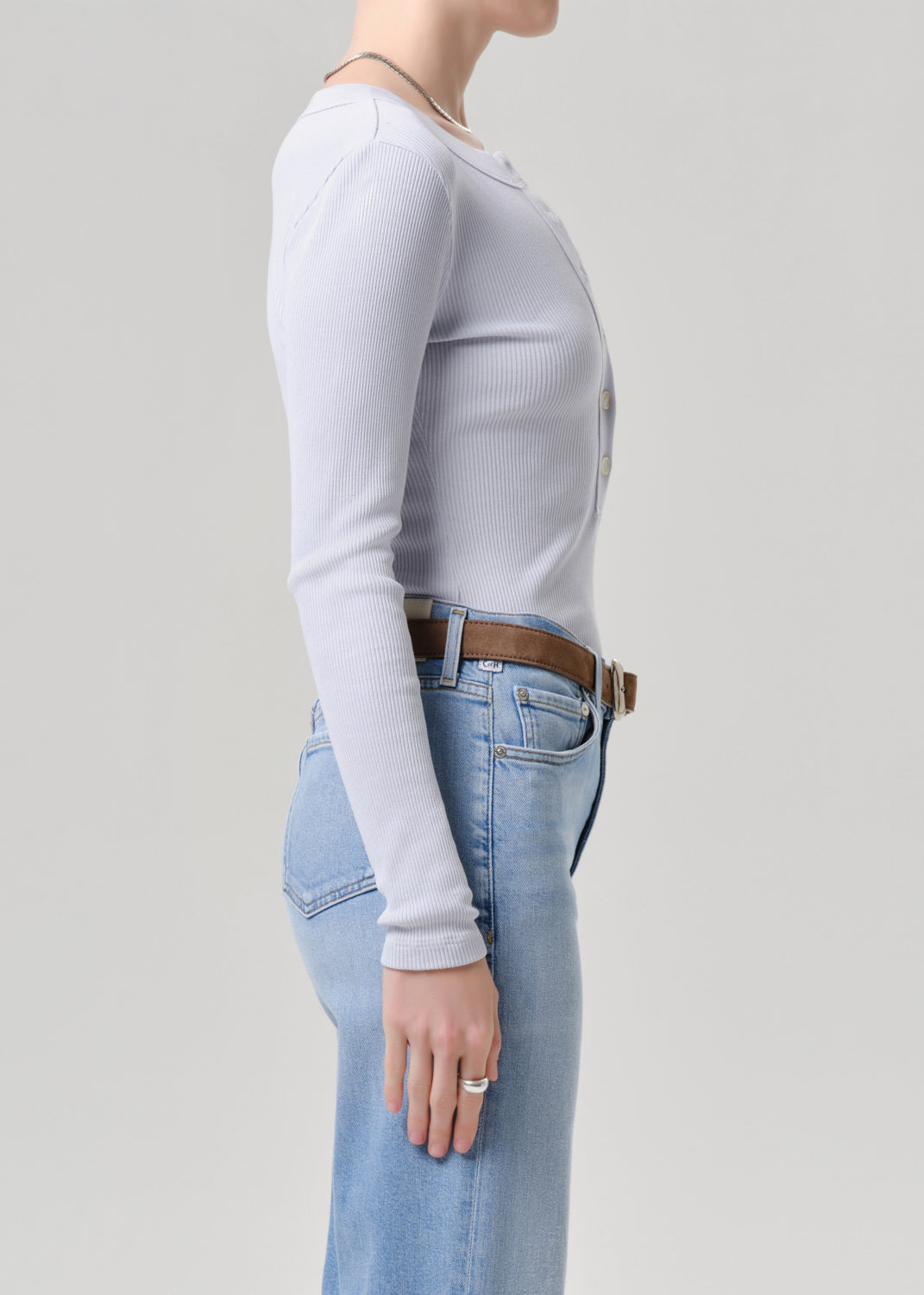 Person wearing a light blue long-sleeve top and blue jeans on a grey background