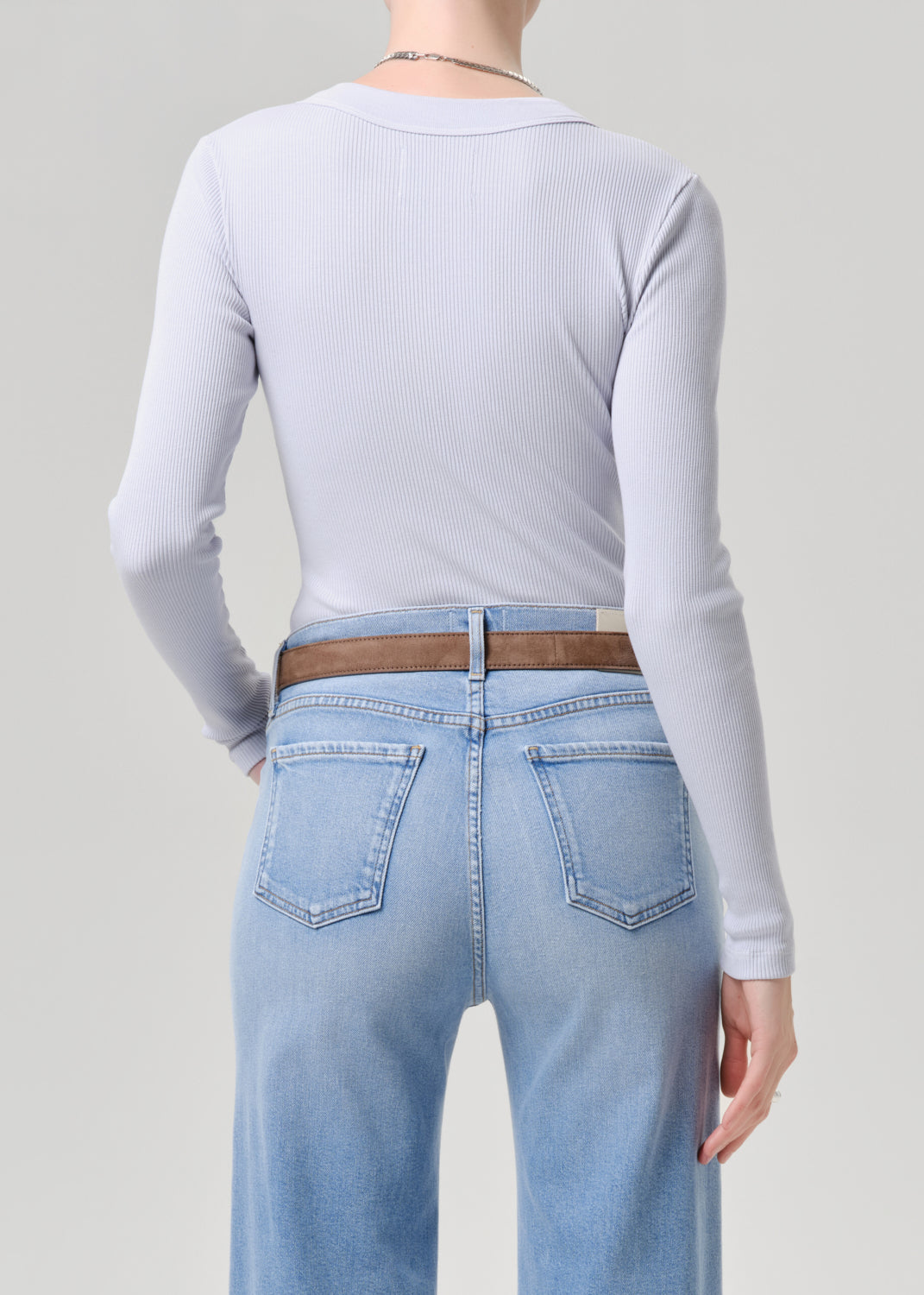 Person wearing a light blue long-sleeve top and light blue jeans on a grey background