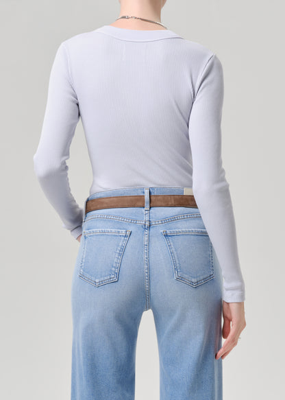 Person wearing a light blue long-sleeve top and light blue jeans on a grey background
