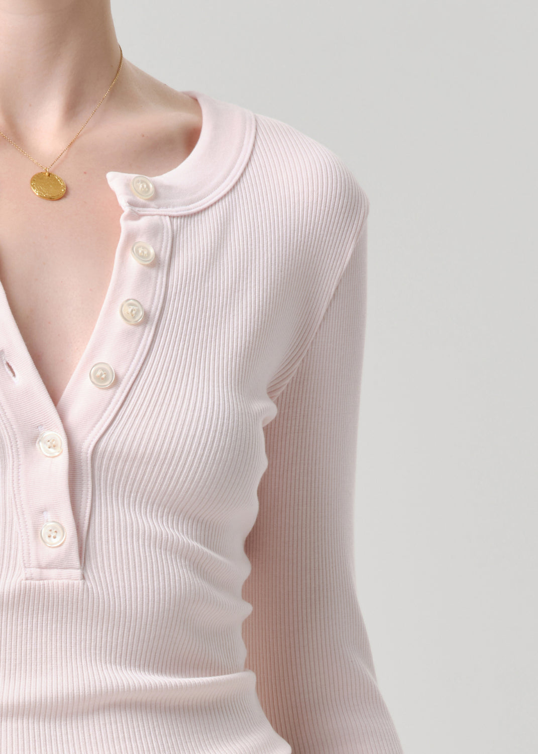 Close-up of a person wearing a light pink long-sleeve top with a necklace on a grey background