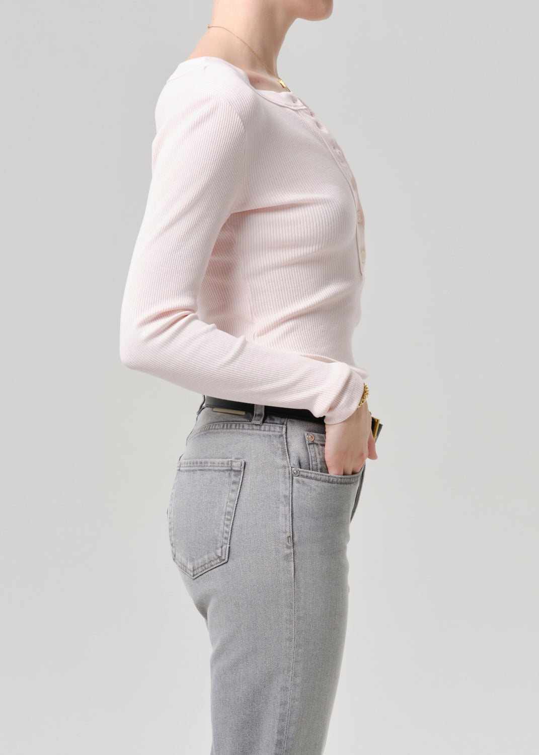 Person wearing a light pink sweater and grey jeans on a grey background