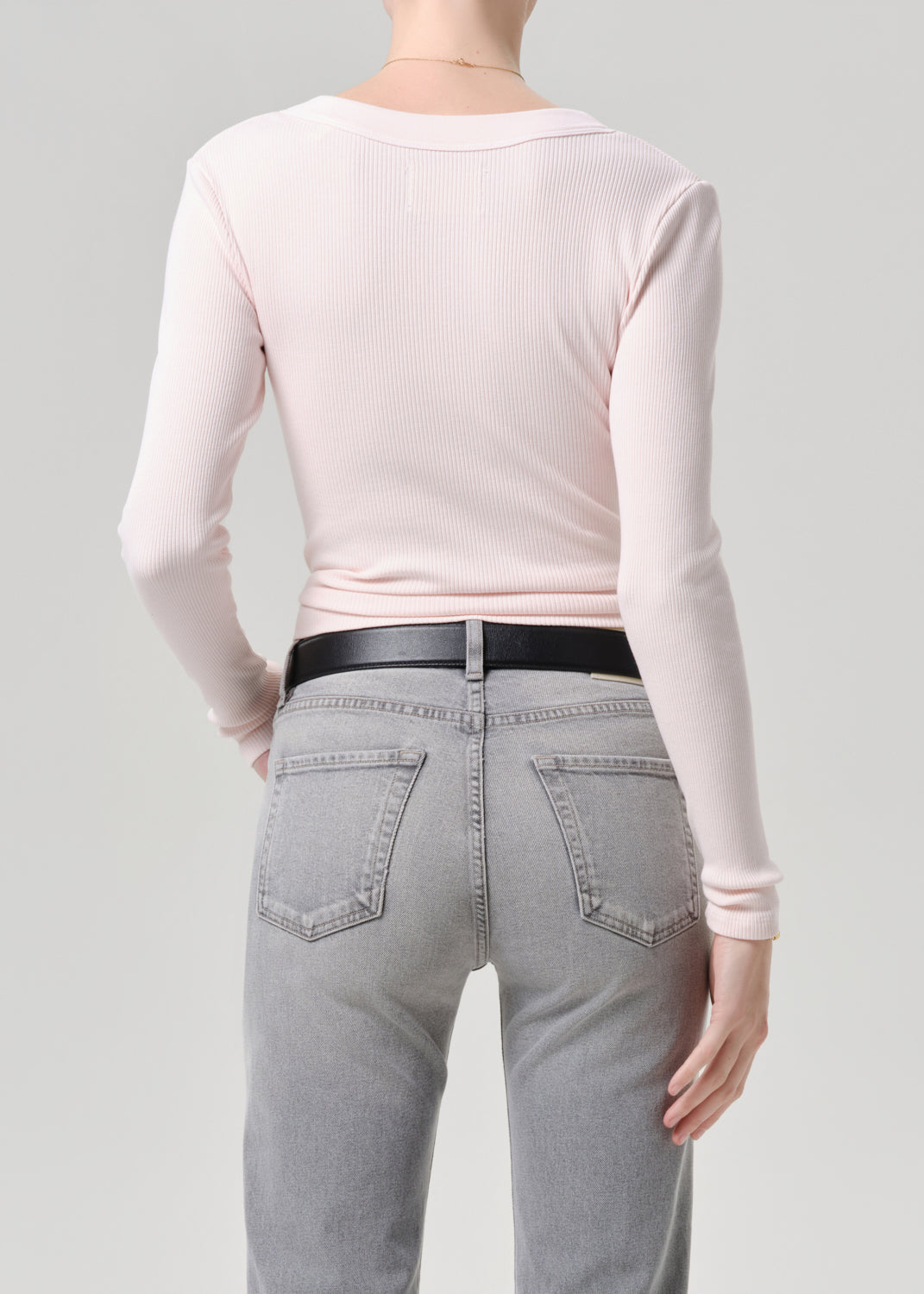 Person wearing a light pink long-sleeve top and grey jeans on a grey background
