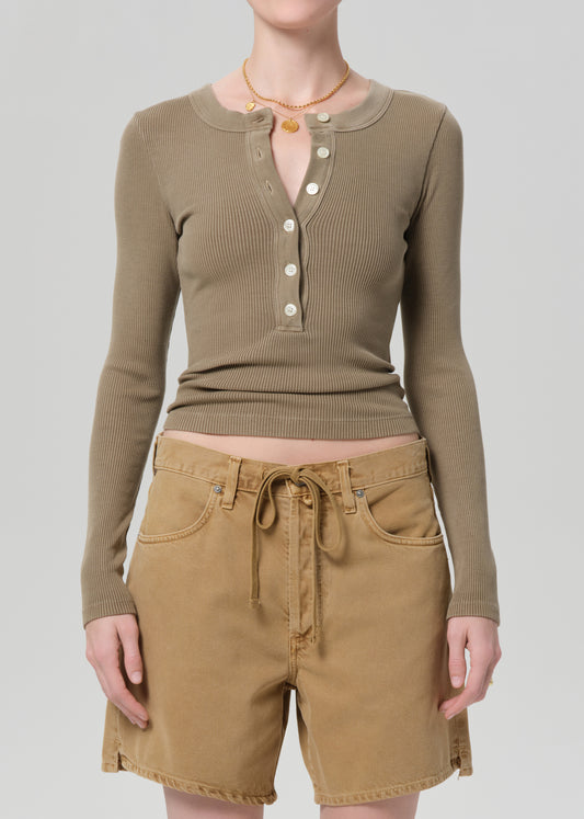 Person wearing a brown long-sleeve top and beige shorts on a plain background