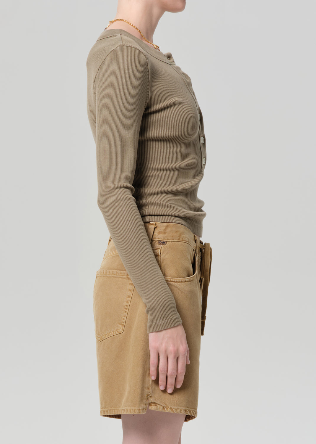 Person wearing a brown long-sleeve top and beige skirt on a light gray background