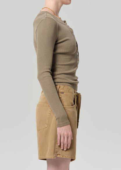 Person wearing a brown long-sleeve top and beige skirt on a light gray background