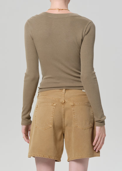 Person wearing a brown long-sleeve top and beige shorts on a white background