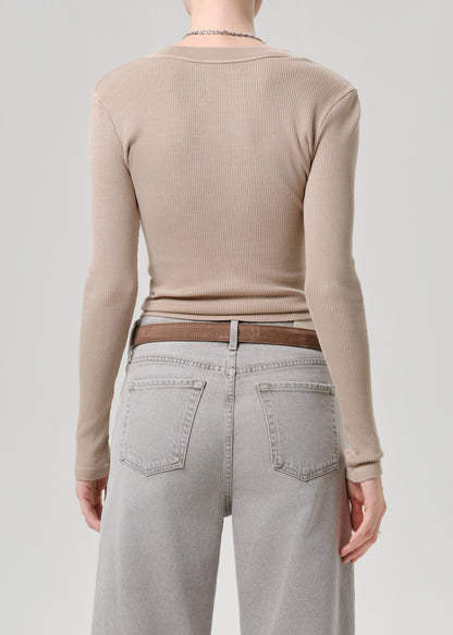 Rear view of a model wearing a beige ribbed long-sleeve top, a brown belt, and light grey jeans against a grey background.