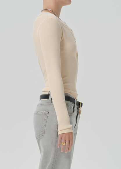 Side profile of a model wearing a beige long-sleeve ribbed knit top tucked into grey jeans with a black belt.