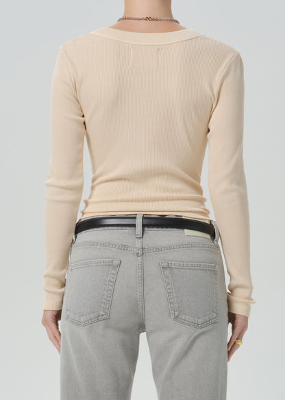 Rear view of a person wearing a light beige ribbed long-sleeve top, light gray jeans, and a black belt against a grey background.