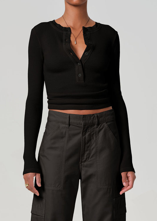 Person wearing a black long-sleeve top and dark pants on a plain background