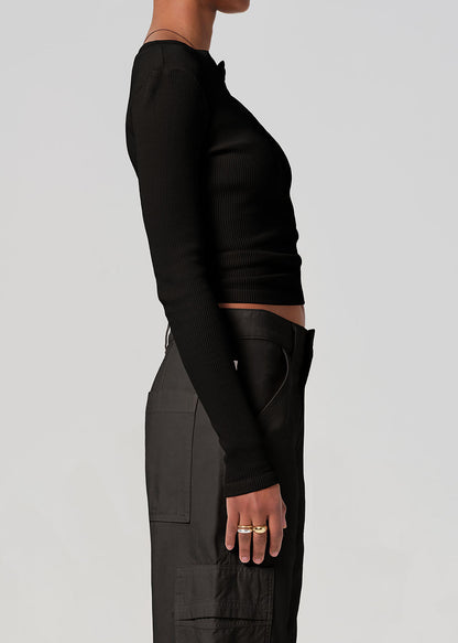 Person wearing a black long-sleeve top and dark pants on a gray background