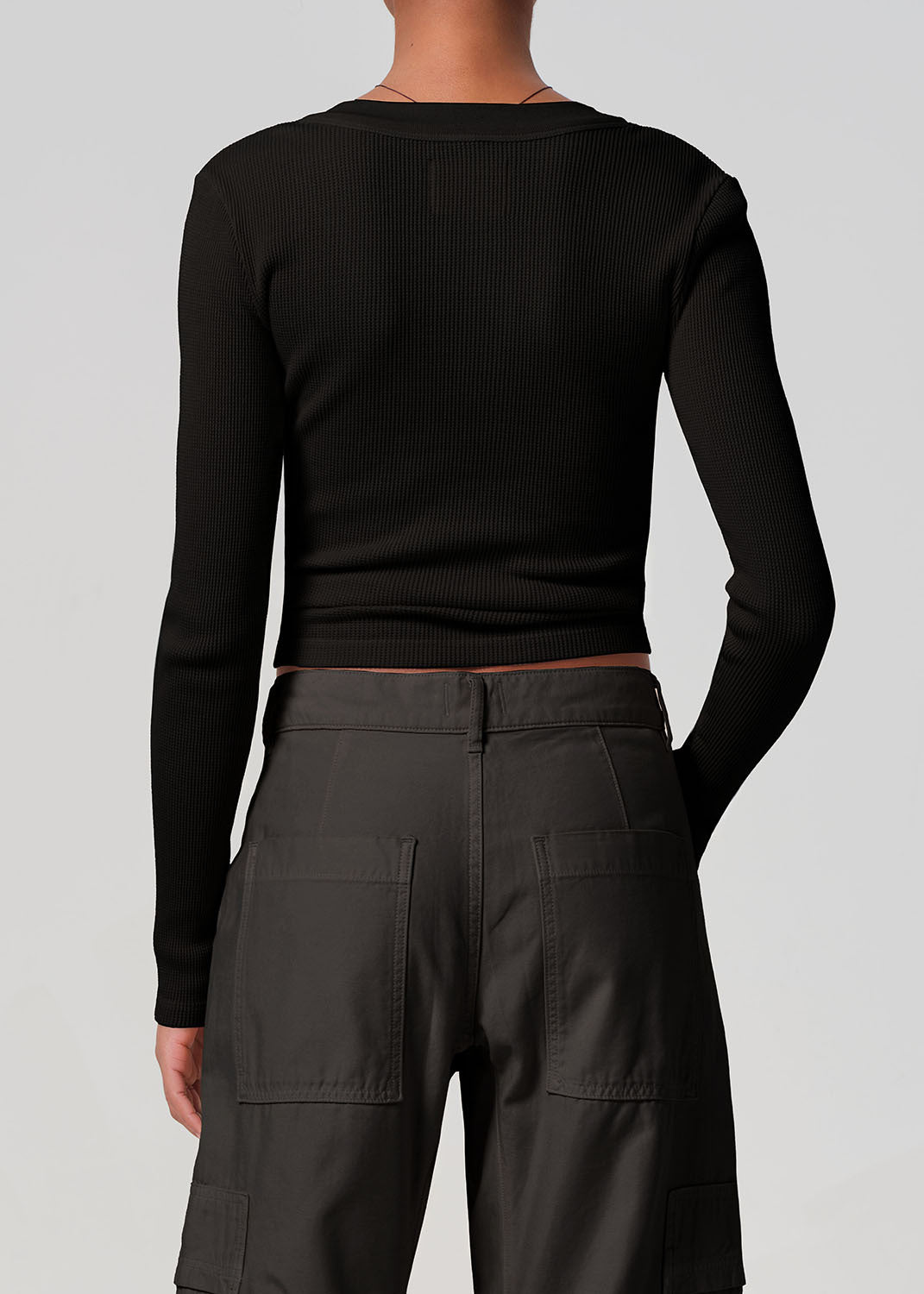 Person wearing a black long-sleeve top and dark cargo pants on a light gray background