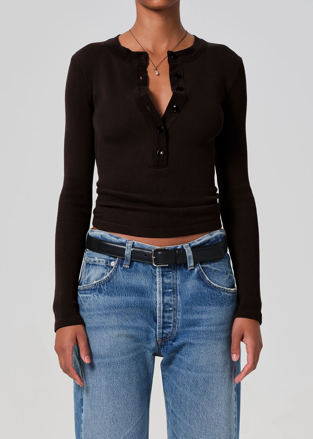 Person wearing a brown long-sleeve top and blue jeans on a gray background