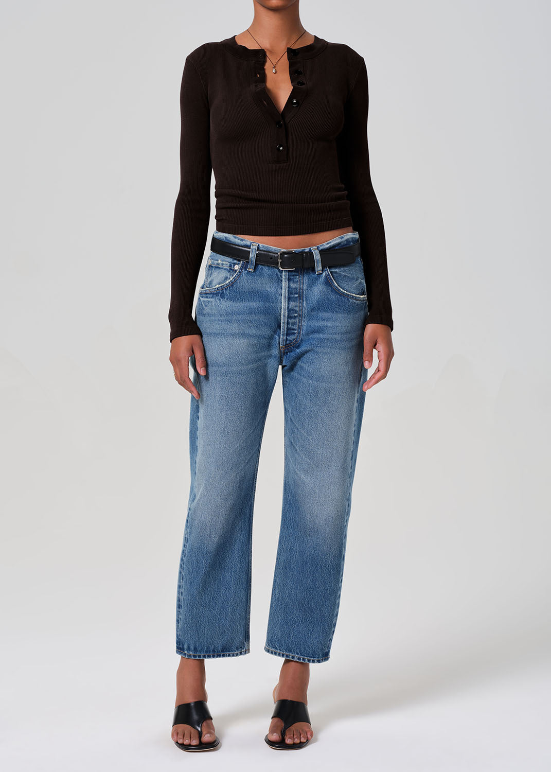 Person wearing a brown long-sleeve top and blue jeans on a gray background