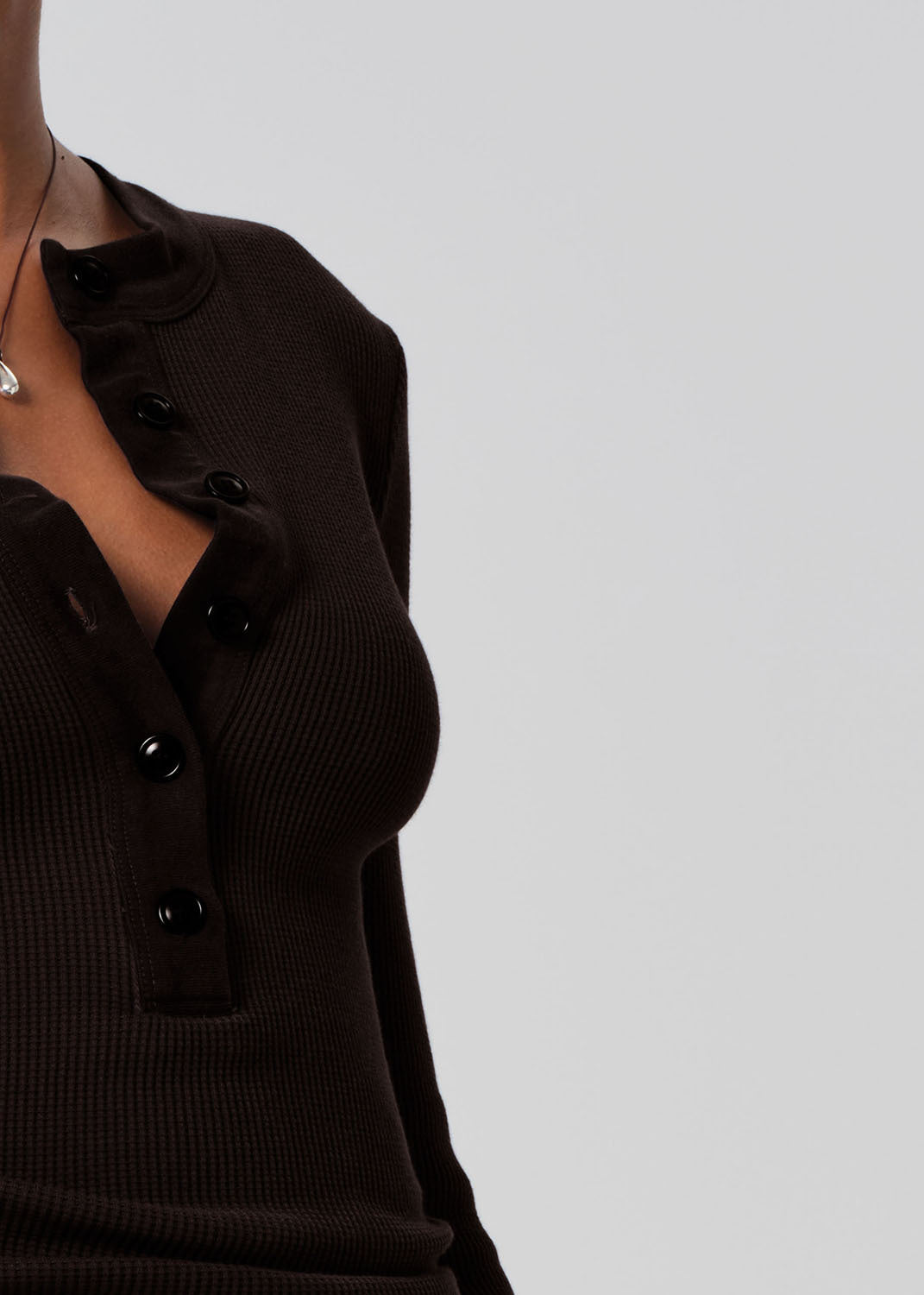 Person wearing a brown long-sleeve top and blue jeans on a gray background