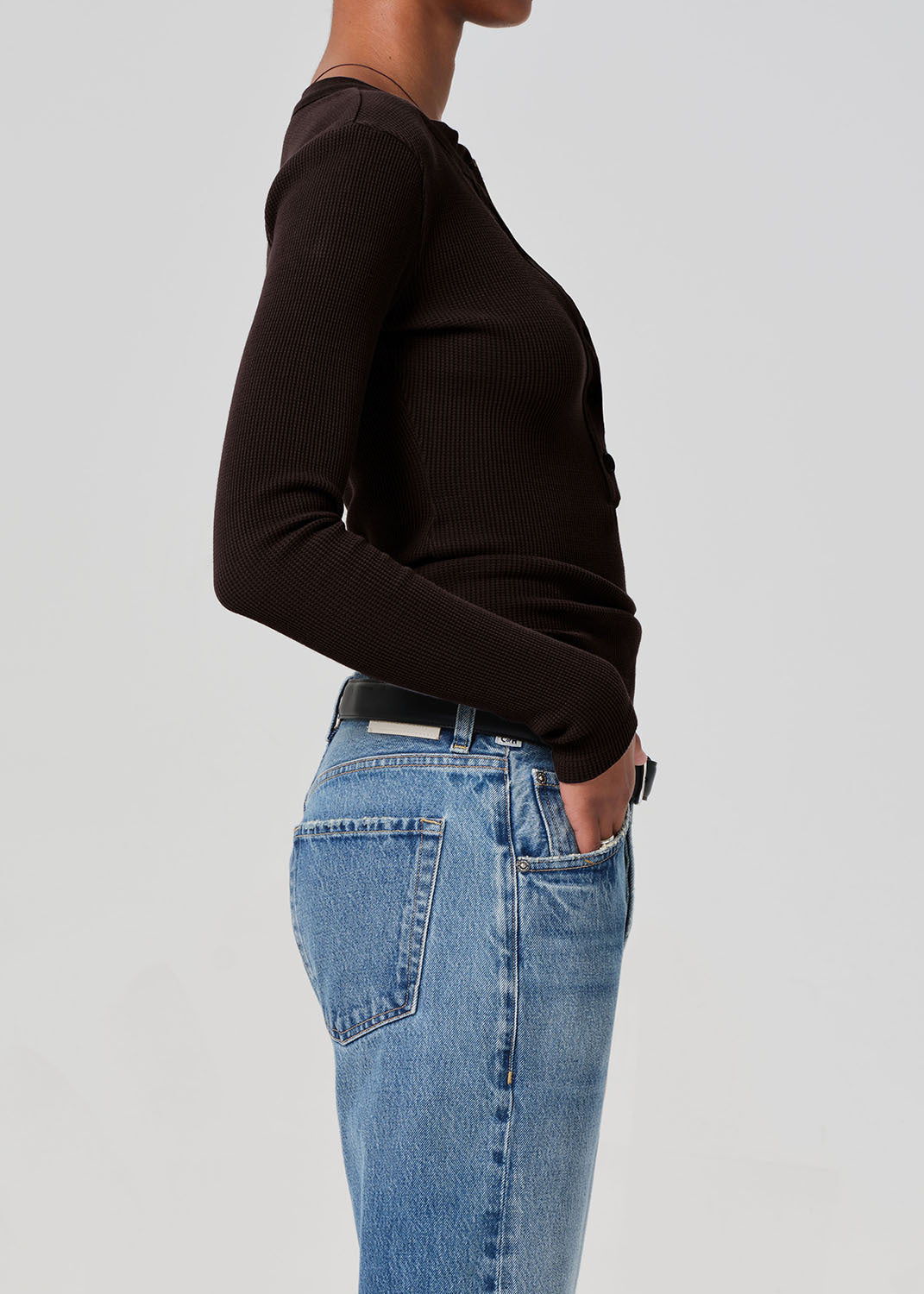 Person wearing a brown long-sleeve top and blue jeans on a gray background