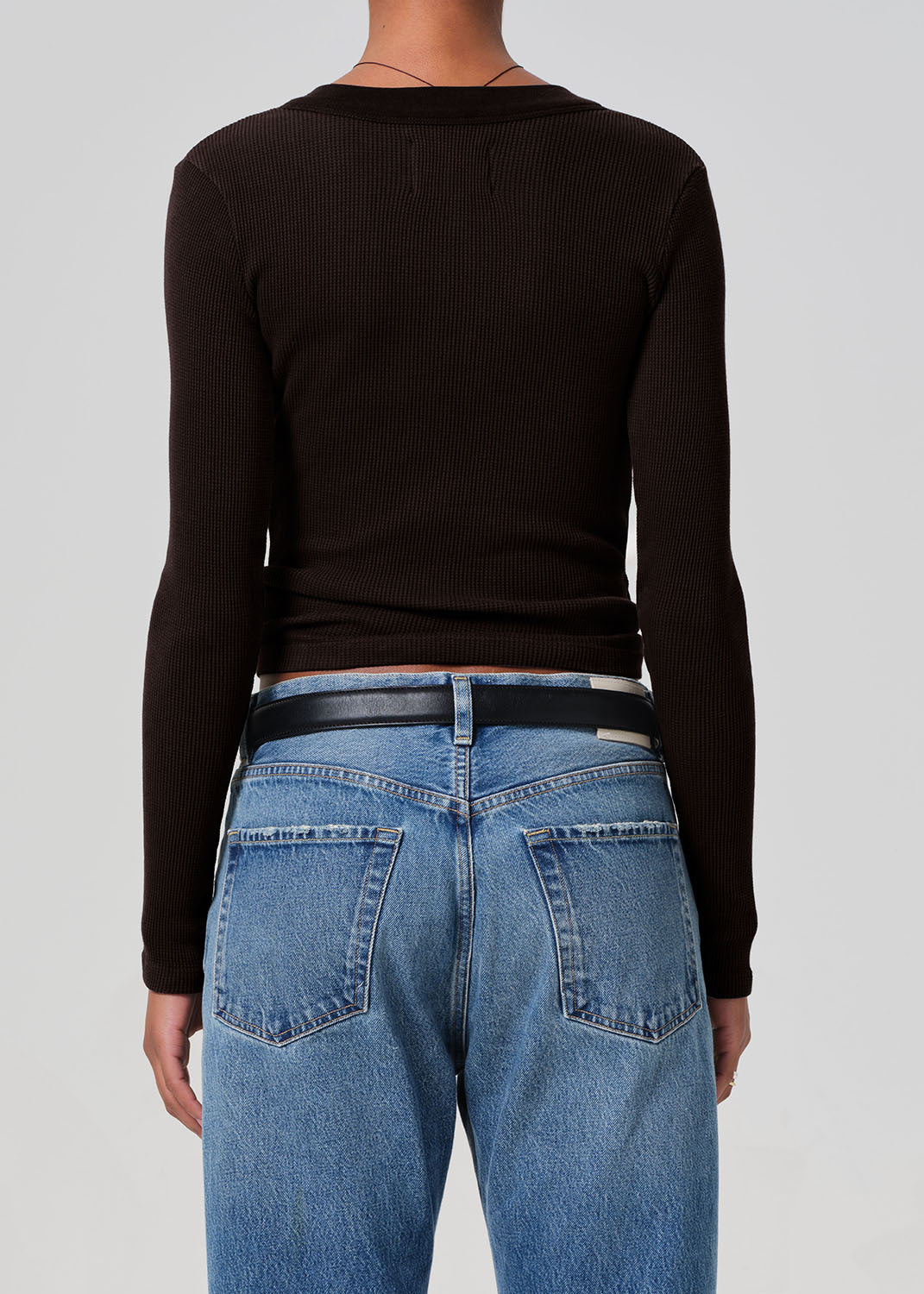 Person wearing a brown long-sleeve top and blue jeans on a gray background