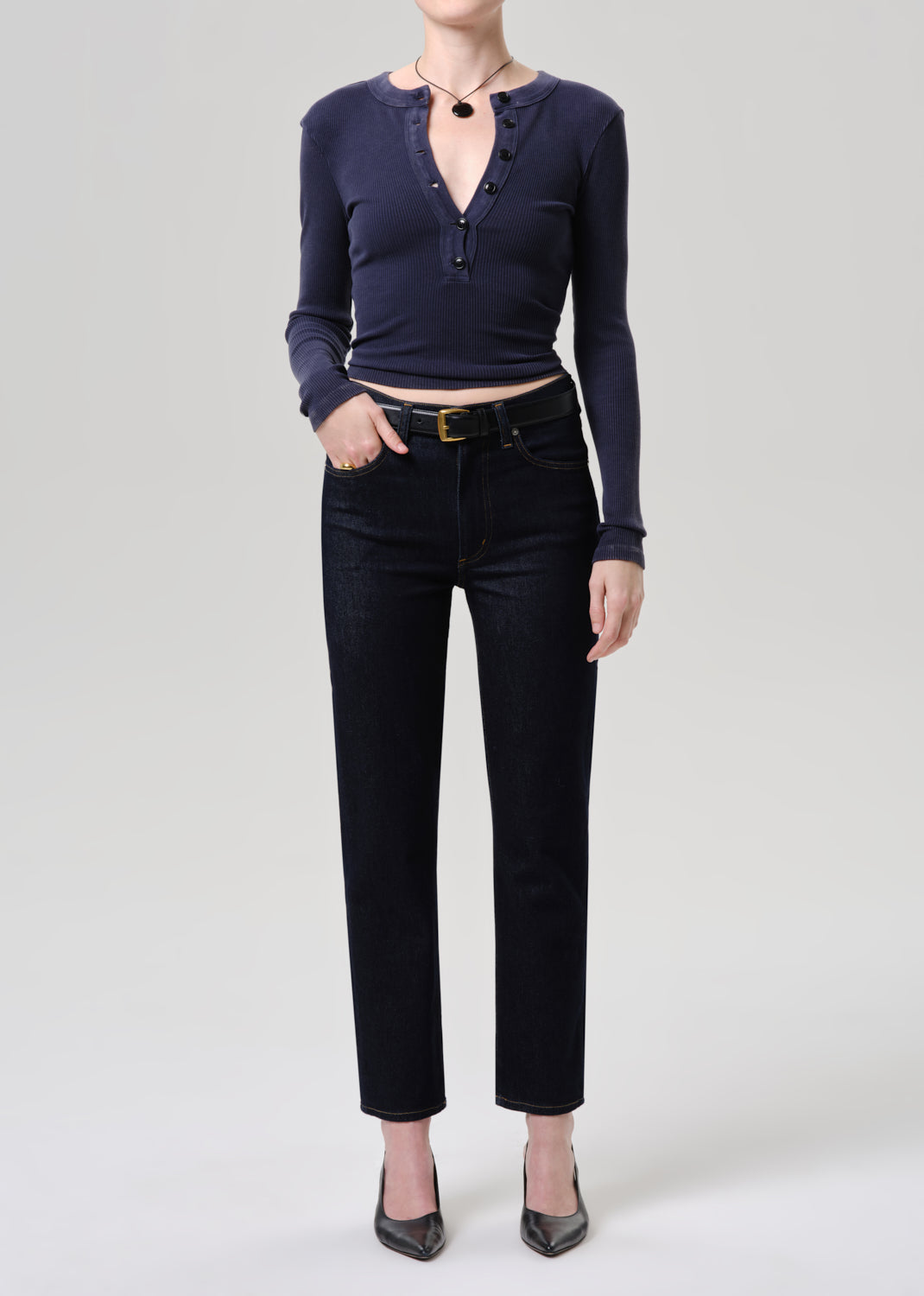 Person wearing a navy long-sleeve top and black pants on a grey background.