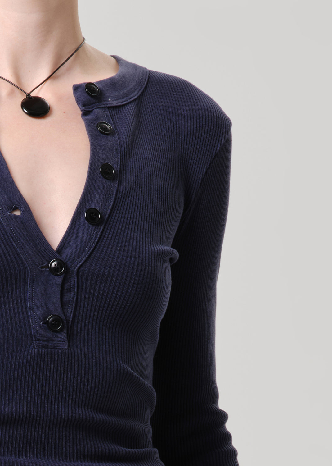 Close-up of a person wearing a dark navy ribbed long-sleeve henley top with black buttons, shown against a grey background.