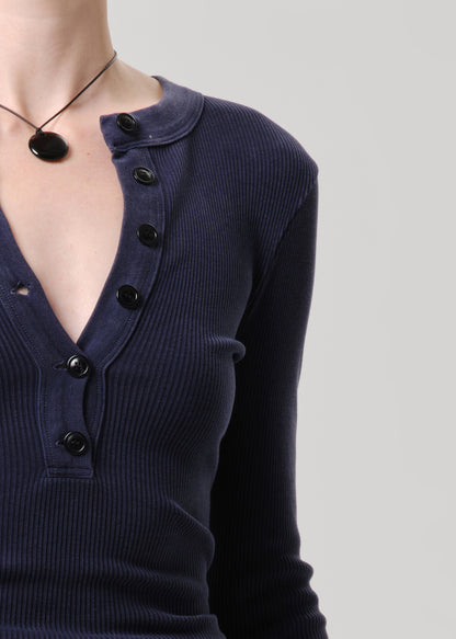 Close-up of a person wearing a dark navy ribbed long-sleeve henley top with black buttons, shown against a grey background.