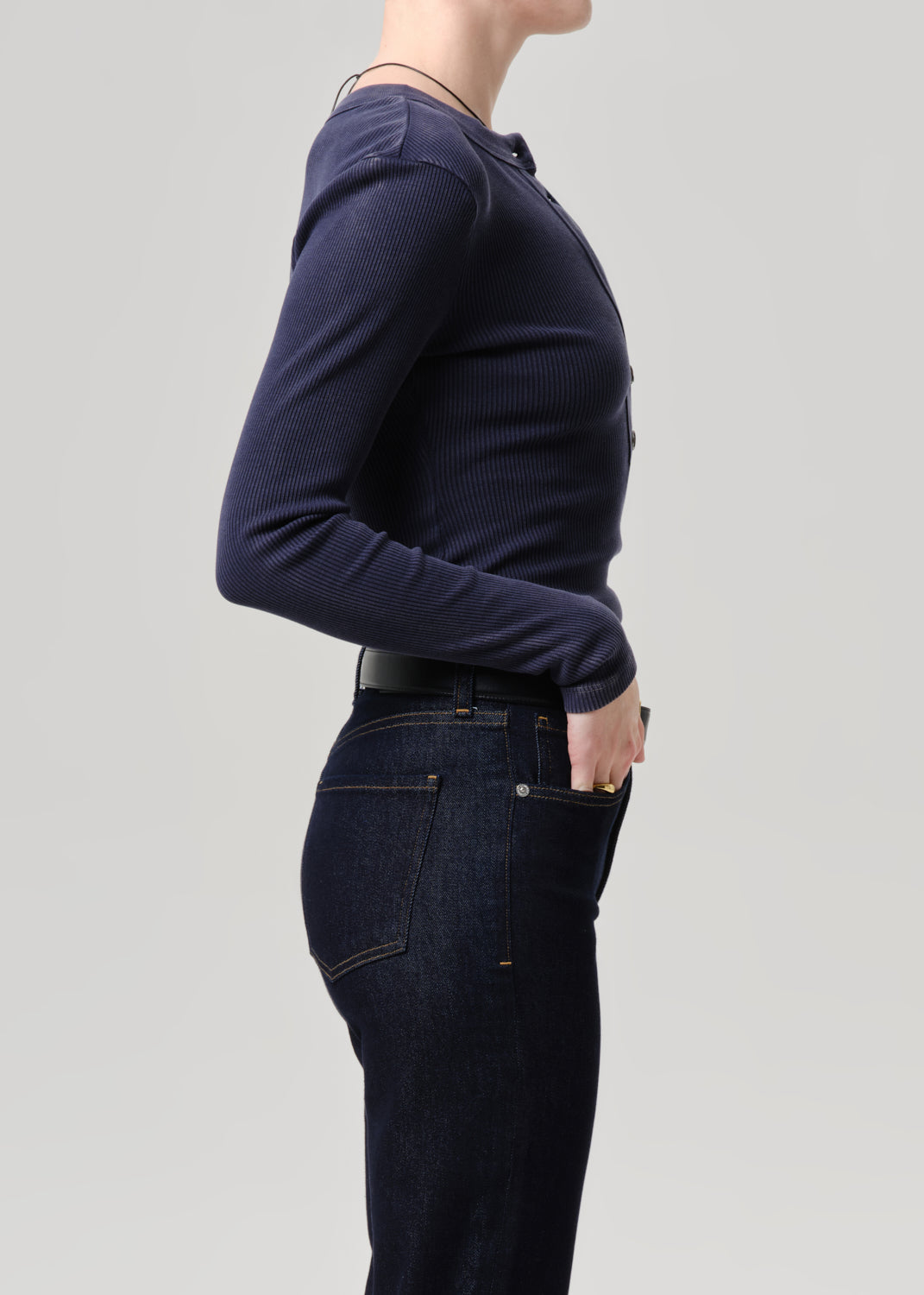 Side profile of a model wearing a dark navy ribbed long-sleeve henley shirt and dark blue jeans against a grey background.