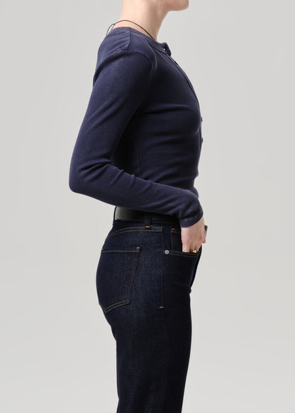 Side profile of a model wearing a dark navy ribbed long-sleeve henley shirt and dark blue jeans against a grey background.