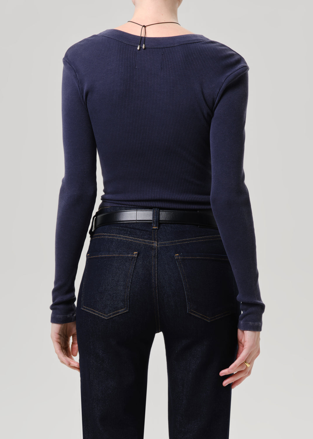 A model shown from the back wearing a dark navy ribbed long-sleeve top tucked into dark blue jeans with a black belt.
