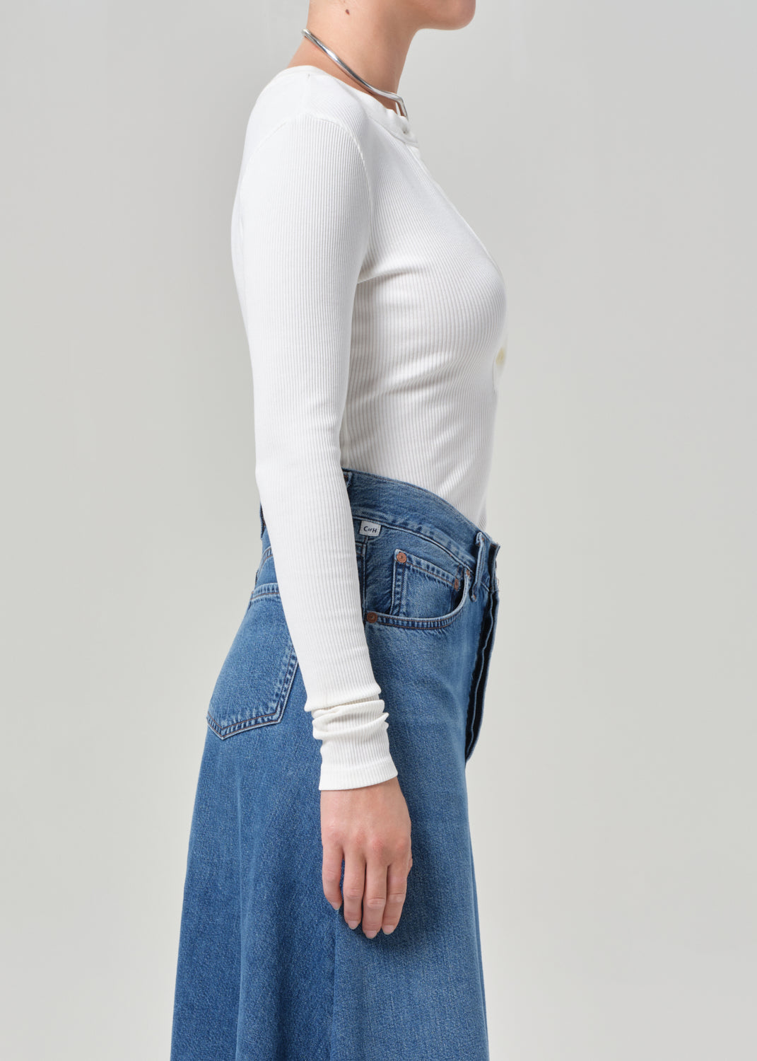 Person wearing a white long-sleeve top and blue jeans on a plain background