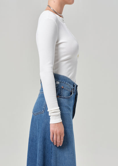 Person wearing a white long-sleeve top and blue jeans on a plain background