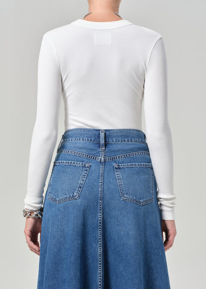 Person wearing a white long-sleeve top and blue denim skirt on a gray background